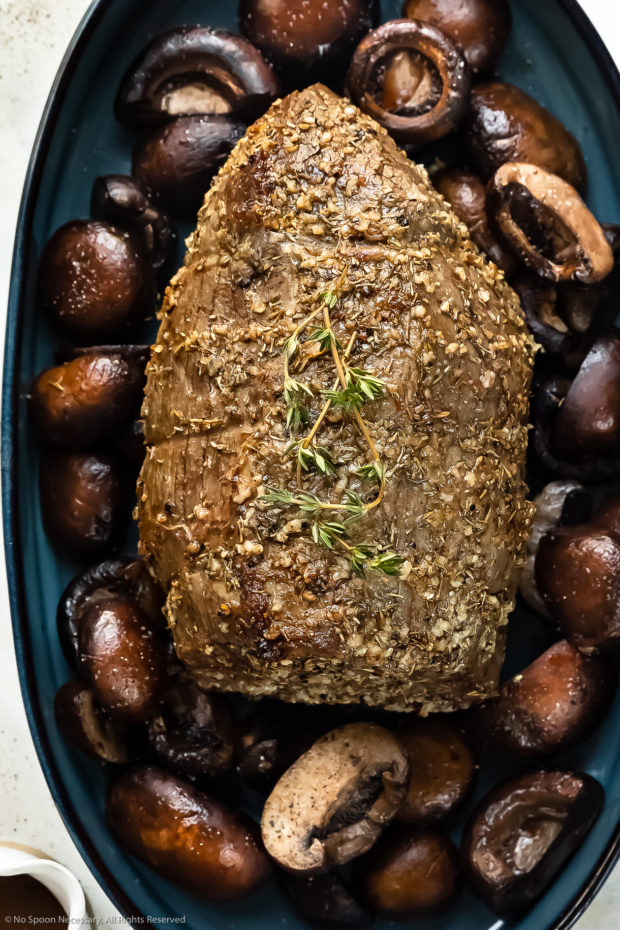 Overhead photo of a roasted whole eye of round beef roast on a bed of mushrooms in a blue roasting pan.