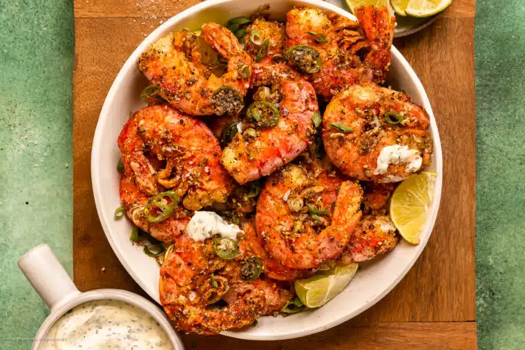 Overhead photo of fried salt and pepper shrimp in a white bowl with a bowl of creamy cilantro dipping sauce off to the side.