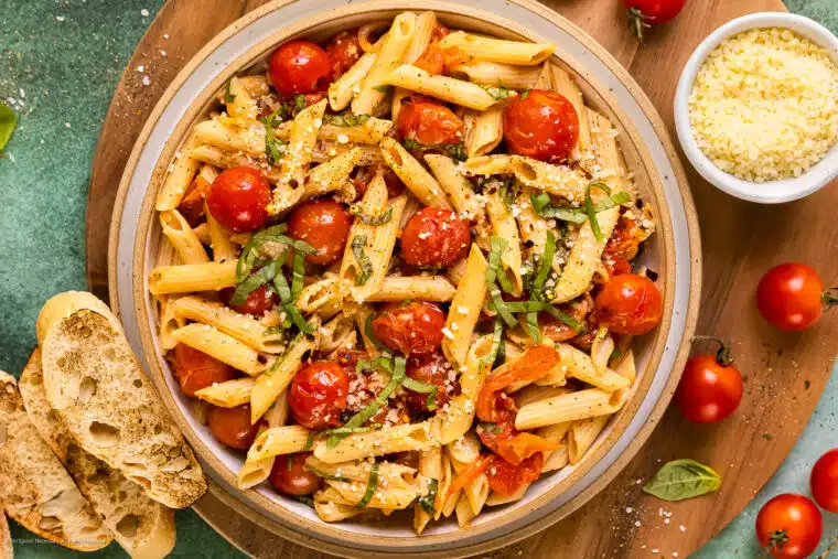 Overhead photo of cherry tomatoes pasta with fresh basil and parmesan cheese in a large serving bowl.
